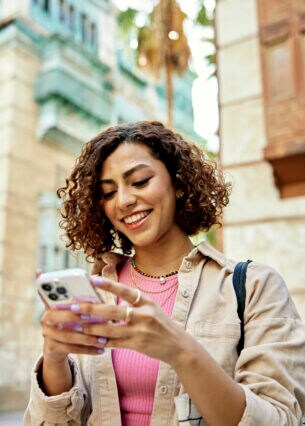 Eine Person steht zwischen hohen Steingebäuden und blickt auf das Smartphone in ihren Händen.
