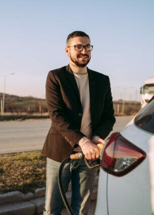 Eine Person steht vor ihrem Auto und hält den Zapfhahn fest, der im Auto steckt.
