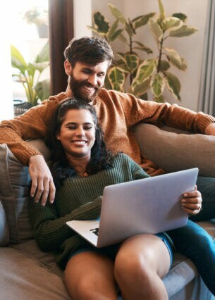 Zwei Personen sitzen gemeinsam auf einem Sofa und blicken in ein geöffnetes Notebook.