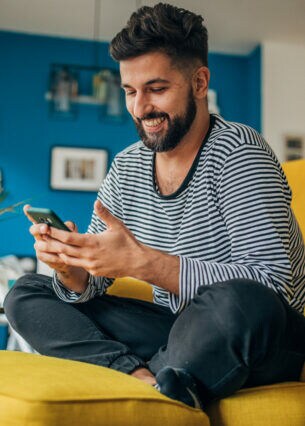 Eine Person sitzt im Schneidersitzt auf einem Sessel und blick auf das Smartphone in ihren Händen.