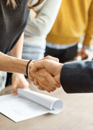 Personen schütteln die Hand über einem Tisch, auf dem Dokumente liegen.