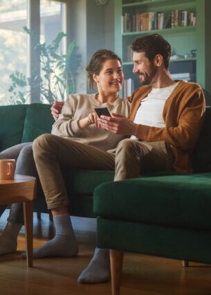 Zwei Personen sitzen nebeneinander auf einem Sofa und blicken gemeinsam auf ein Smartphone.