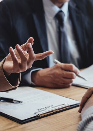 Nahaufnahme eines Verhandlungstisches an dem sich mehrere Personen unterhalten.