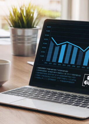 Ein aufgeklappter Laptop, auf dessen Display Diagramme abgebildet sind, steht auf einem Konferenztisch neben einer Kaffeetasse.