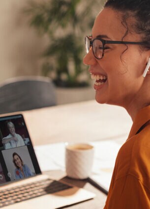 Frau sitzt in einem Online Meeting und lacht.