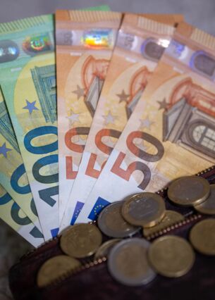 Geldscheine mit dem Wert von 100 und 50 Euro stecken in einem Geldbeutel, während auf dem Geldbeutel Münzen liegen. (zu dpa: «Jeder Dritte kann sich Abkehr vom Bargeld vorstellen»)