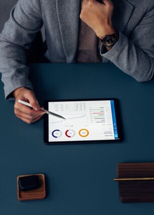 Artikelbild Person sitzt vor Tablet am Schreibtisch und analysiert die Zahlen auf dem Tablet