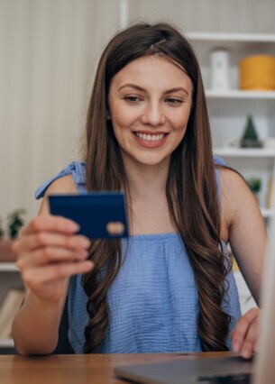 Frau kauft etwas am Laptop und hält eine Karte dabei in der Hand