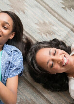 Mother and daughter laying on carpet using cell phone and digital tablet