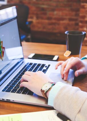 Person arbeitet an einem Laptop in einem modernen Büro mit Notizblock, Smartphone und Teetasse auf dem Schreibtisch