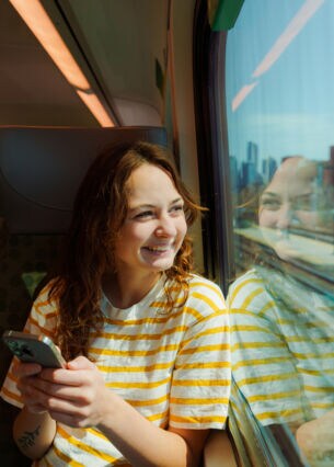 Person sitzt in der Bahn am Handy und schaut aus dem Zugfenster