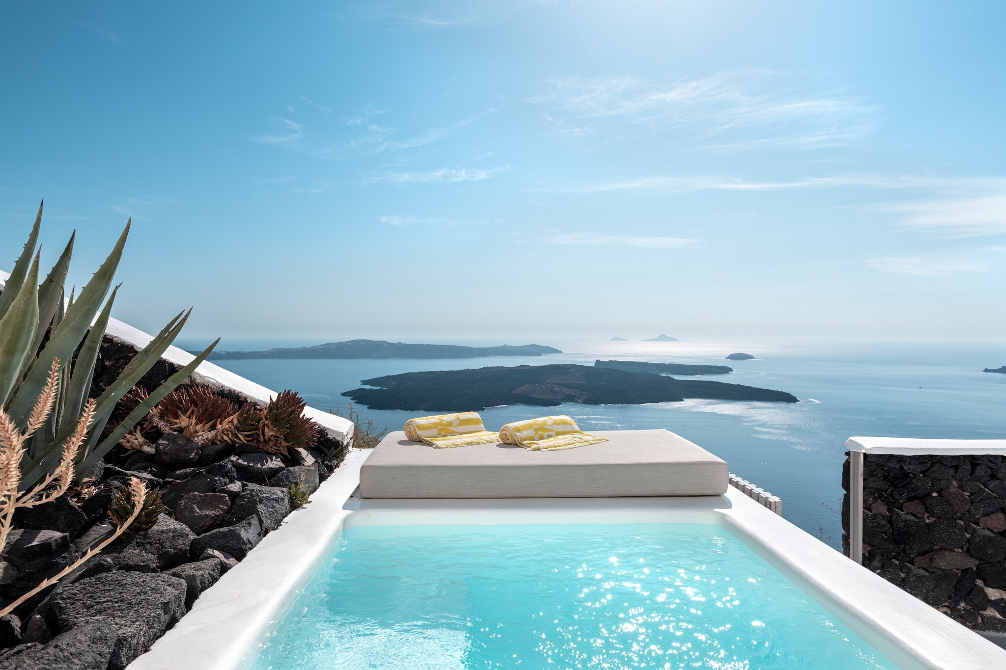 A private balcony plunge pool overlooks the water and a small island beyond. A lounge mat is set up nearby with two yellow-and-white towels.