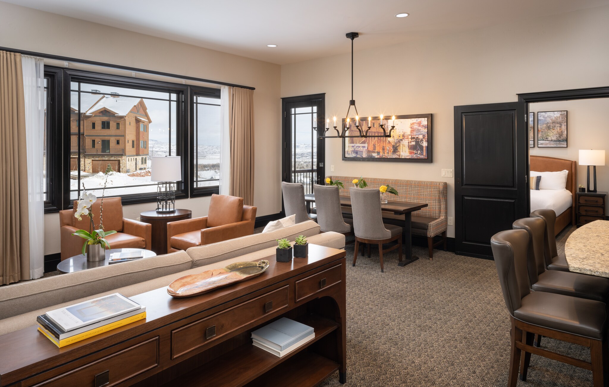 A residence living and dining area is decorated in warm neutral tones, with two casual dining areas and seating overlooking the windows.