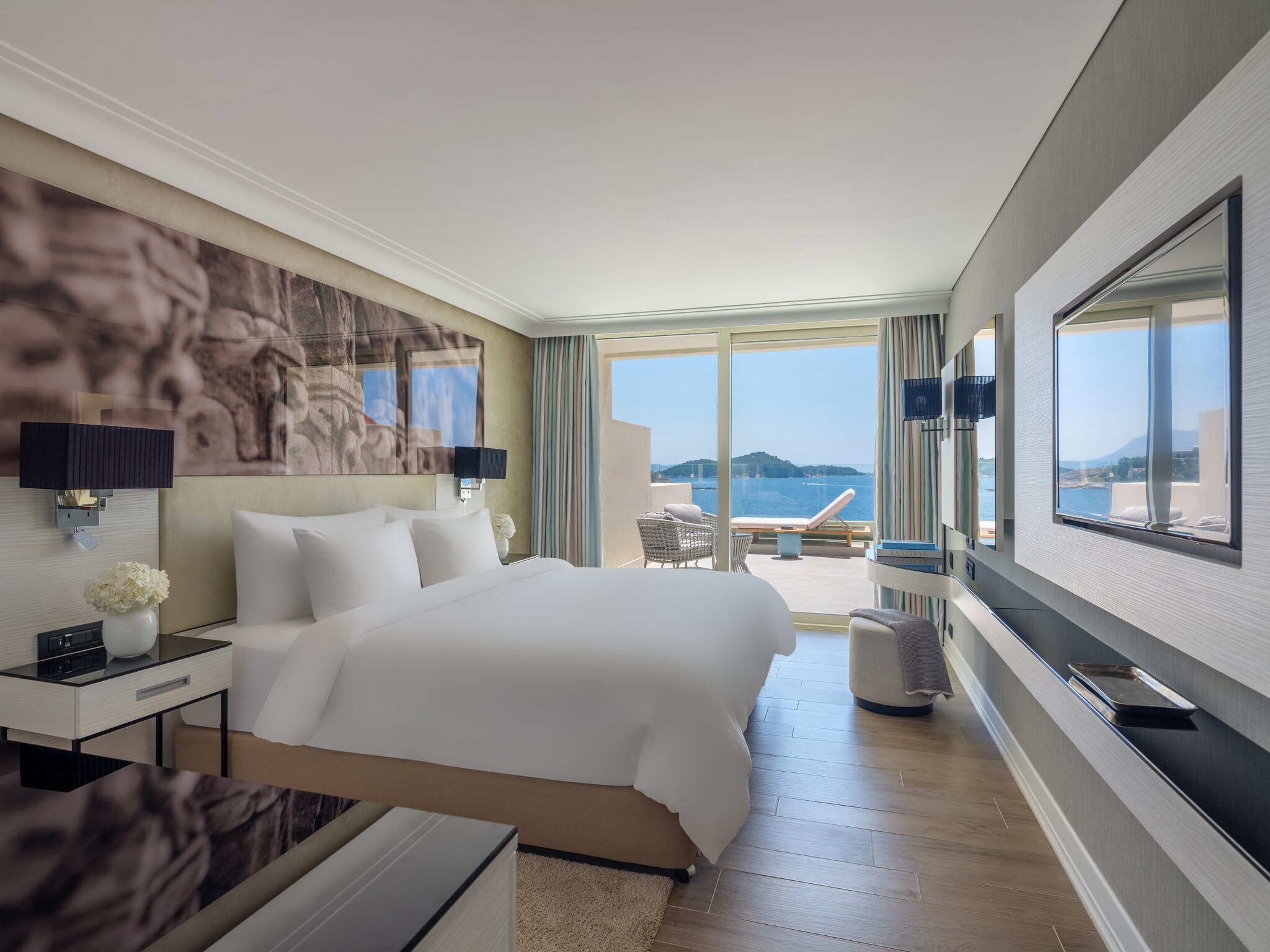 A guest room has a long counter along one wall and a long photo over the bed along the other, with glass doors to a patio on the far end.