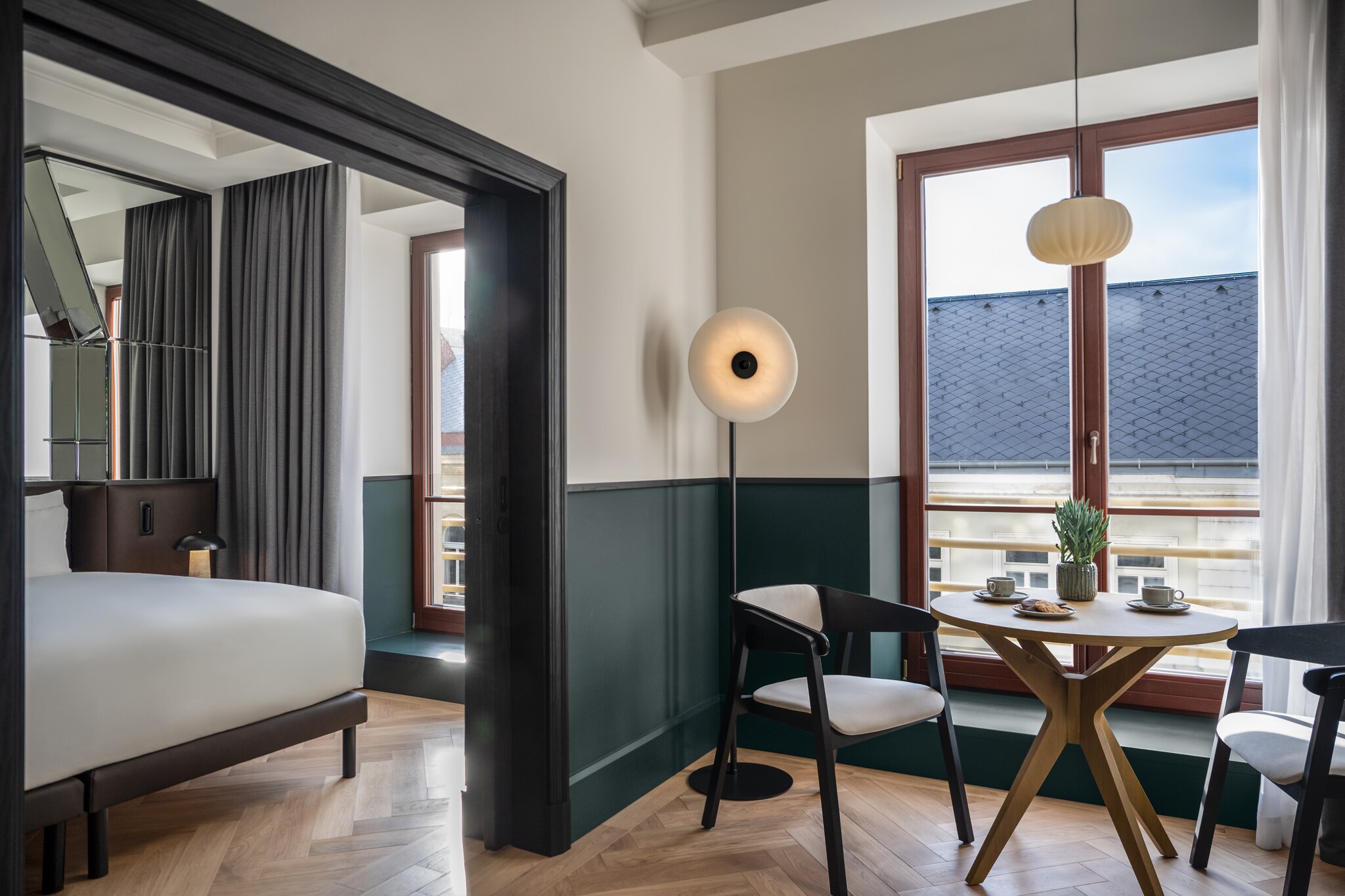 The Executive Suite has a living area with a small table and chairs next to tall windows. Through an arch, mirrors are mounted behind a bed.