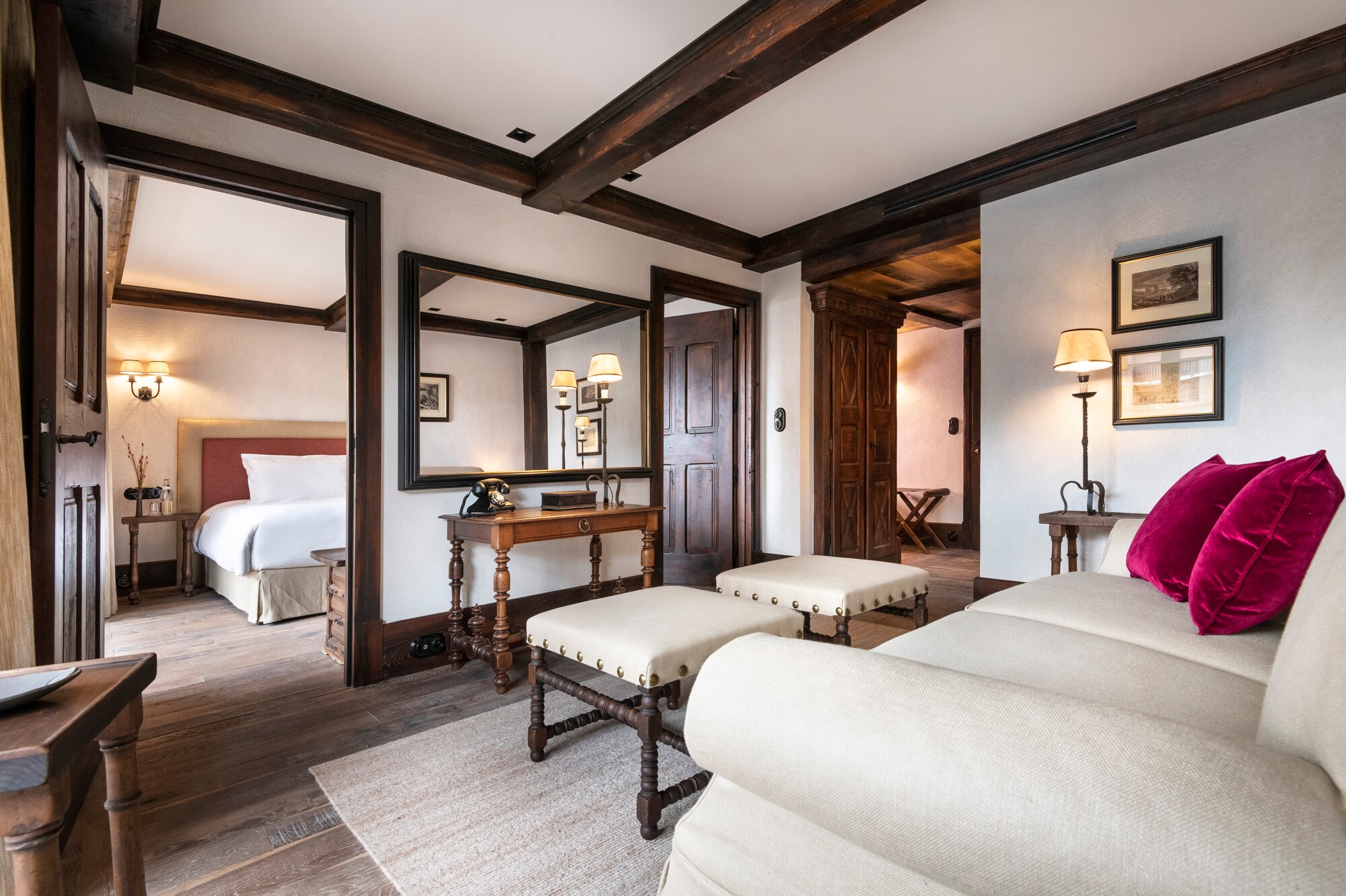In a Junior Suite decorated white with brown trim, a cream couch with red velvet cushions faces a mirror and the doors to the bedroom.