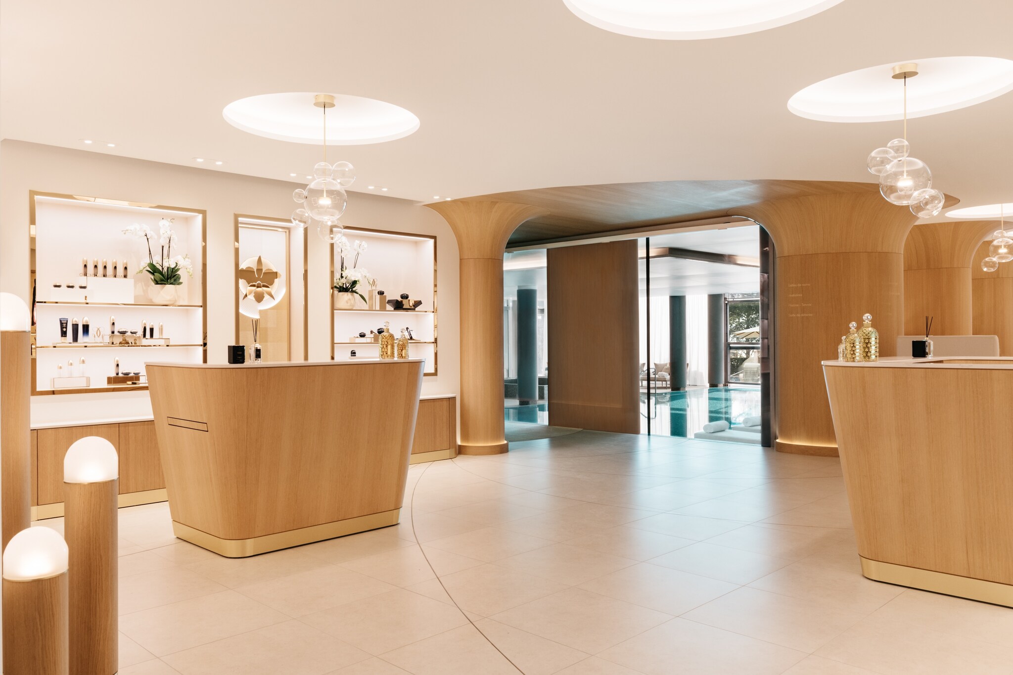 Guerlain Spa is pristine, with white walls and smooth, gently curved wooden furniture. Brightly lit shelves hold orchids and beauty products.