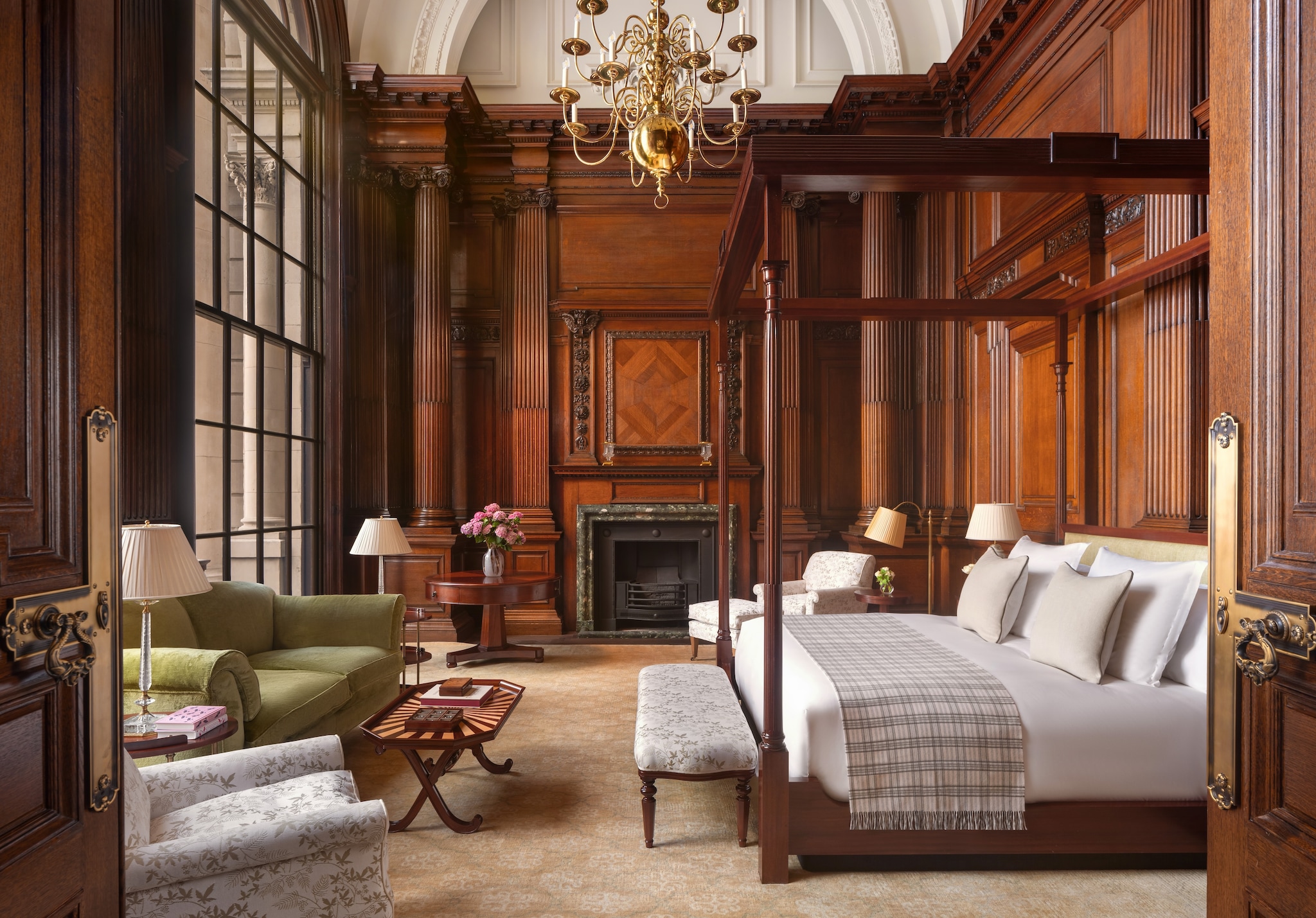 The Granville Suite guest room features a four-poster bed, rich wood paneling, a small green couch, and an ornate chandelier.