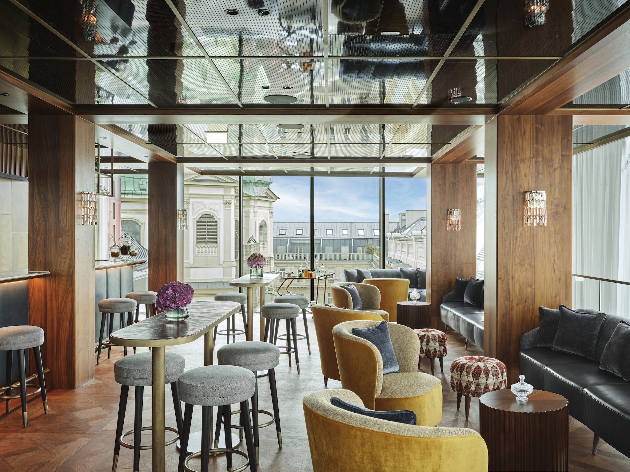 The rooftop brasserie Neue Hoheit Bar is filled with high-top tables, stools, and leather booths surrounded by floor-to-ceiling windows.