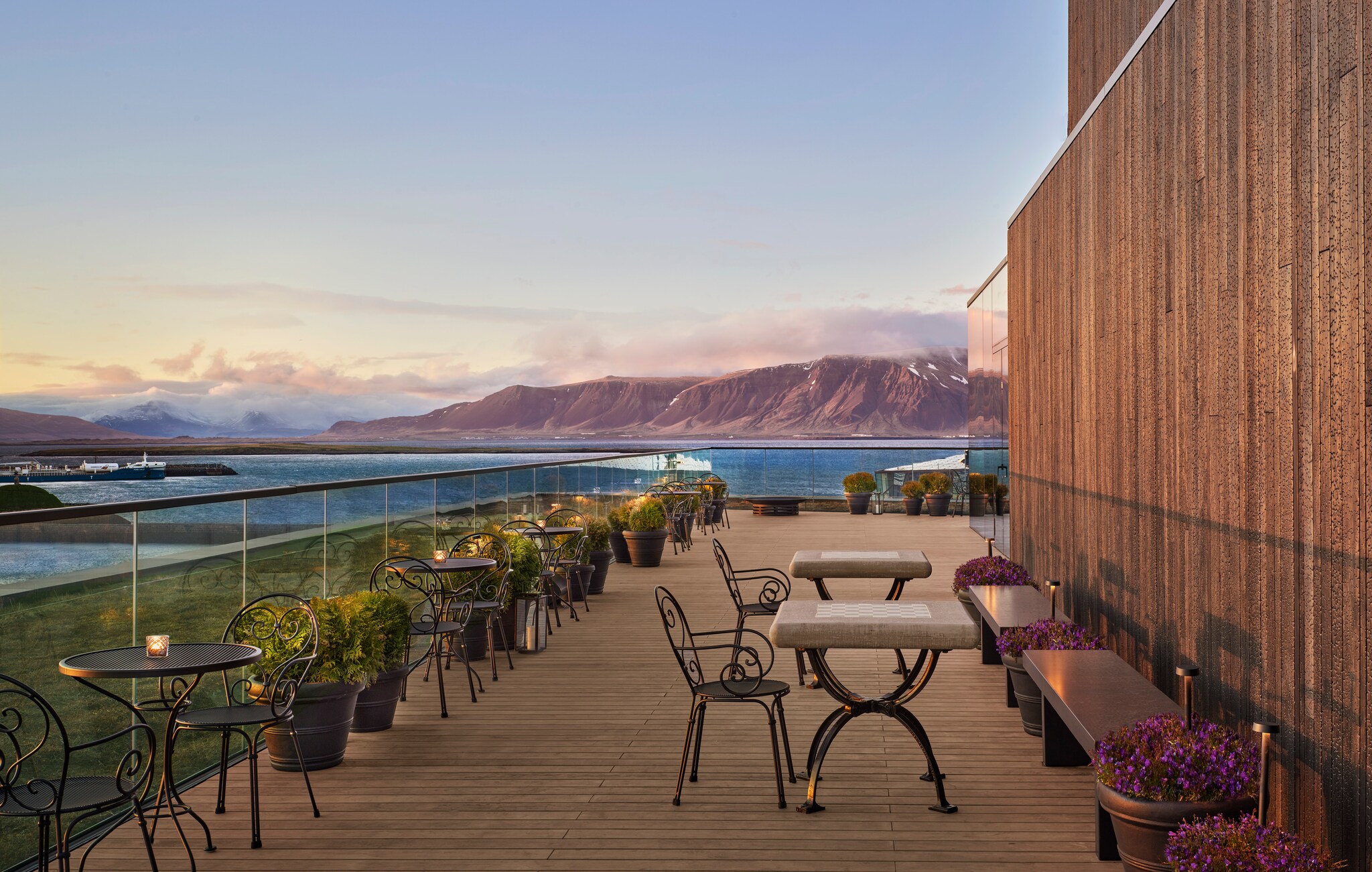 The terrace at the ROOFtop bar is filled with metal tables and chairs punctuated by potted plants. Glass railings offer clear views around.