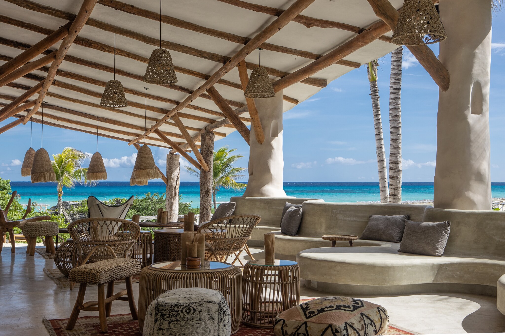 Eolo Beach Club is decorated with woven light fixtures and wicker furniture. The bright waters of the sea are visible through the open walls.