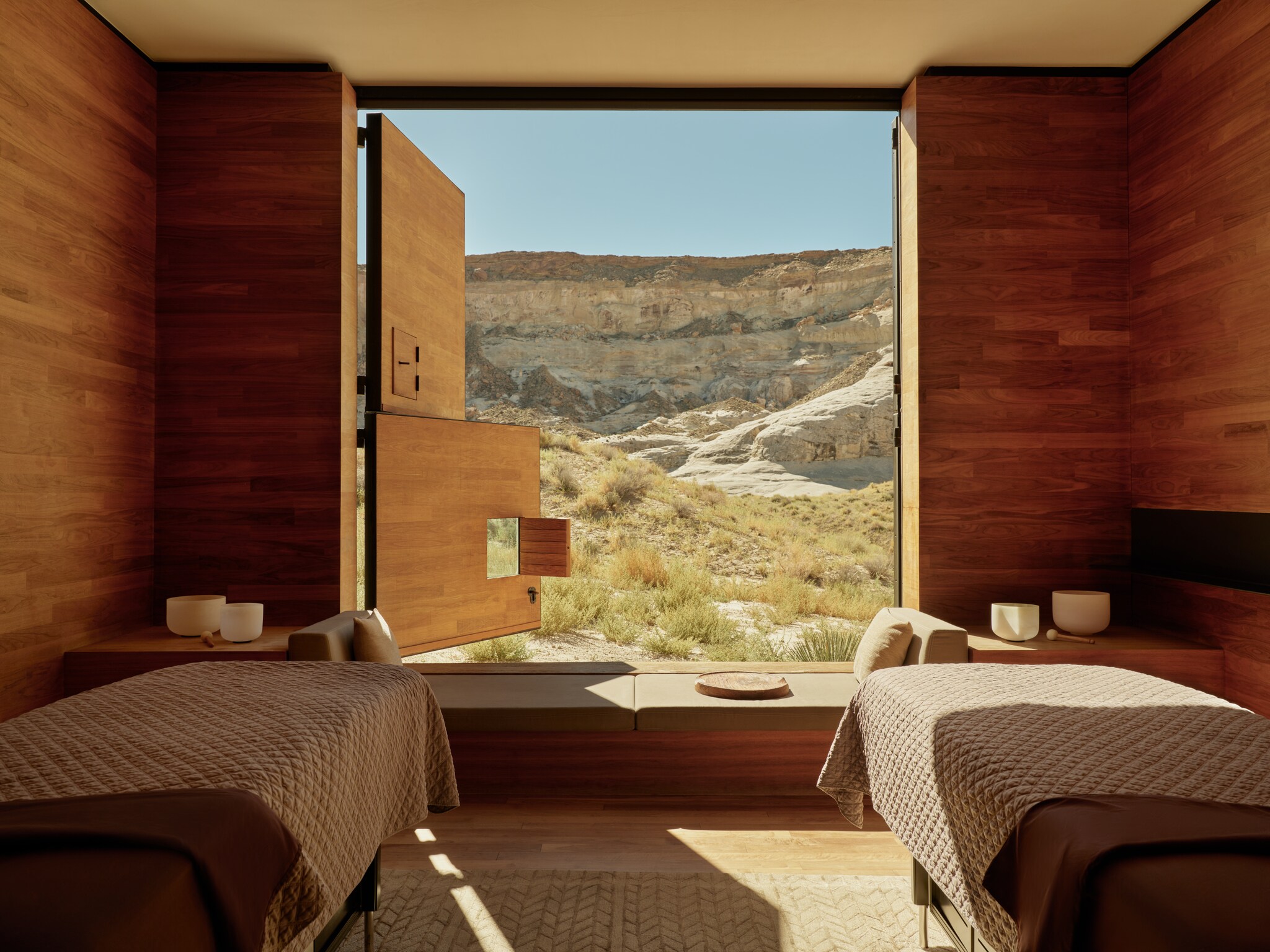 In a spa area with wooden walls and two massage beds covered in quilted blankets, dutch doors swing open to reveal a rocky landscape.