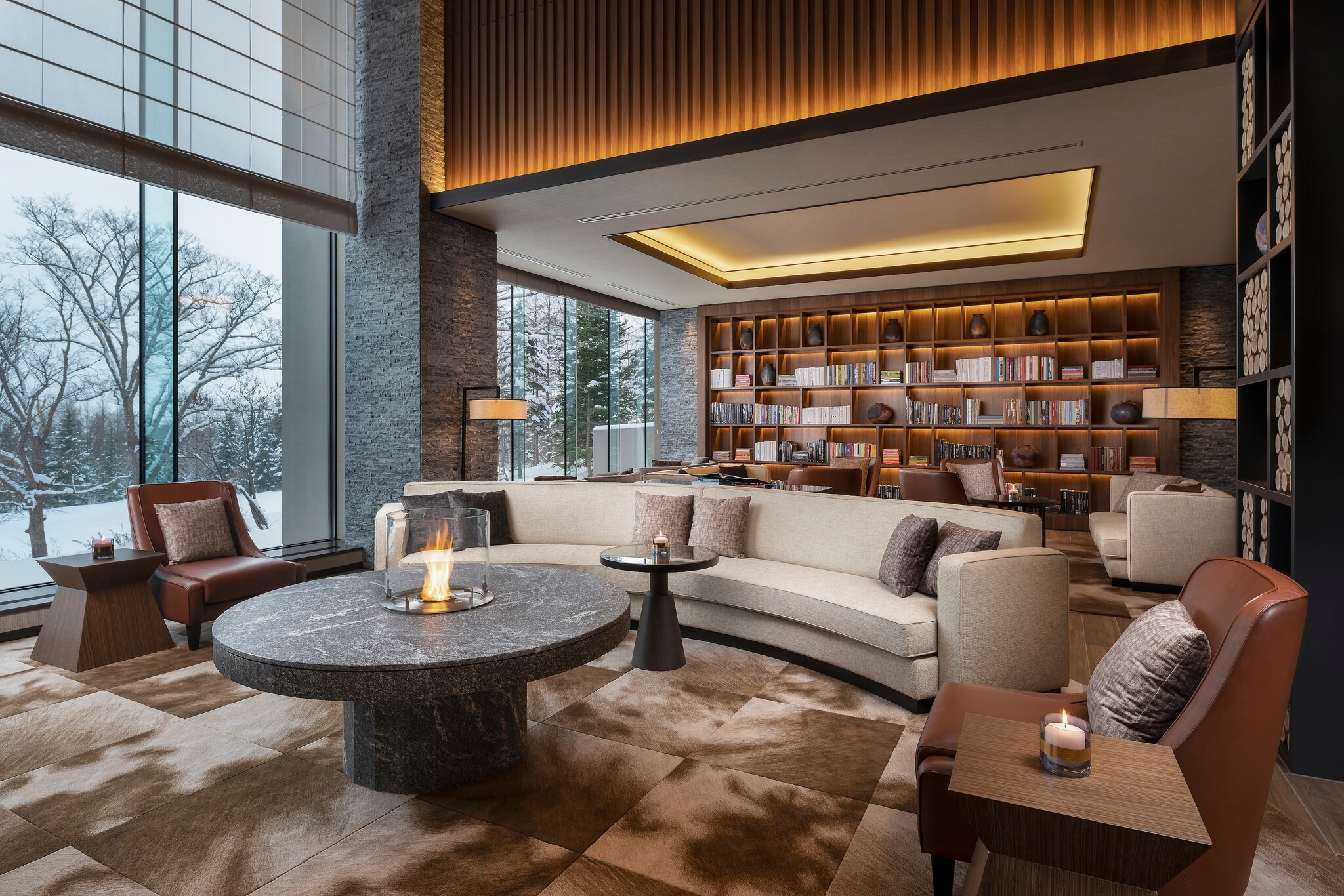 In Ume Lounge, a large, semicircular couch and brown leather armchairs are gathered around a circular table with a fire in the middle.