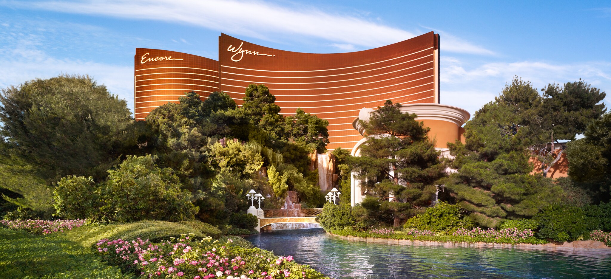 The Wynn and Encore are amber buildings with curved roofs and white stripes along the side. In front, a stream runs between idyllic gardens.
