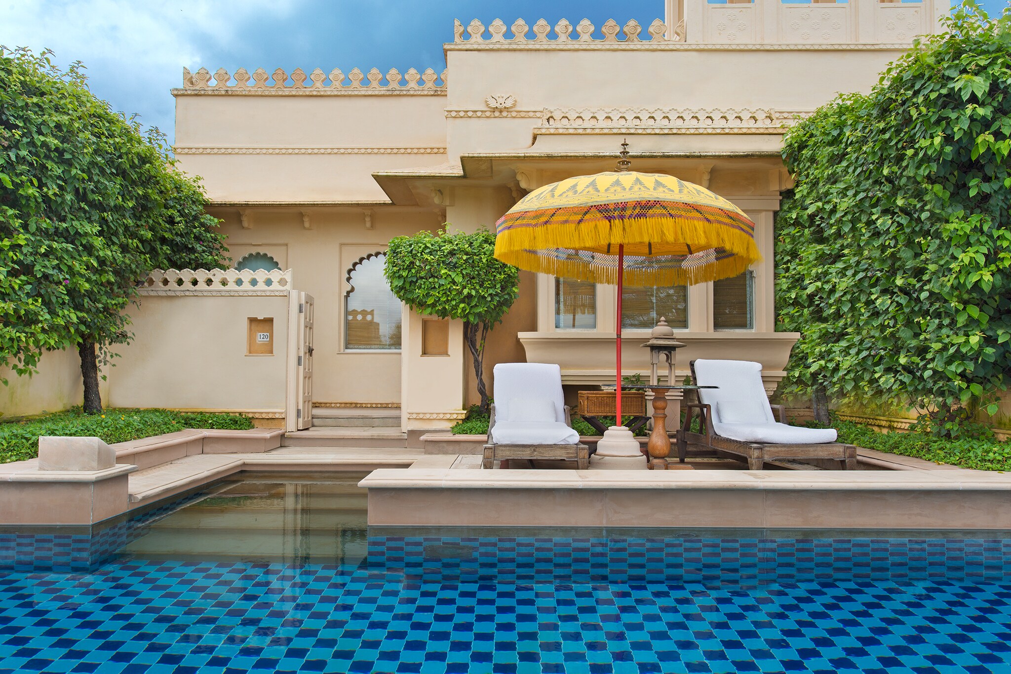 Exterior of a premier room with a semi-private pool. Two sun loungers are arranged under a fringed yellow umbrella in front of the pool.
