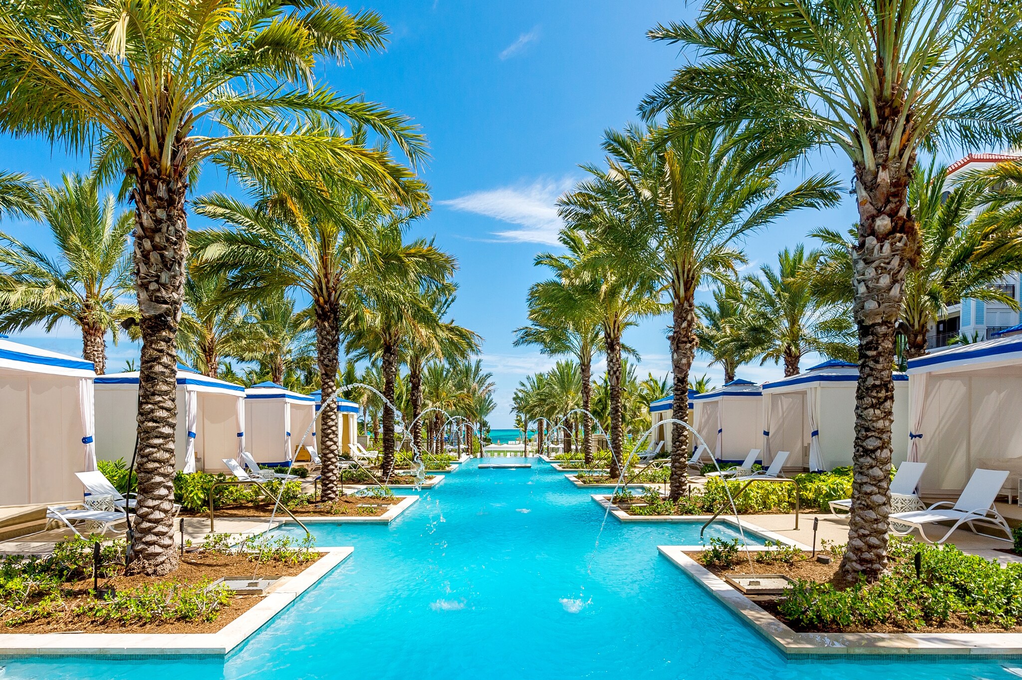 The reflections pool is long and bright blue, fed with arcing fountains and interspersed with cabanas separated by palm trees.
