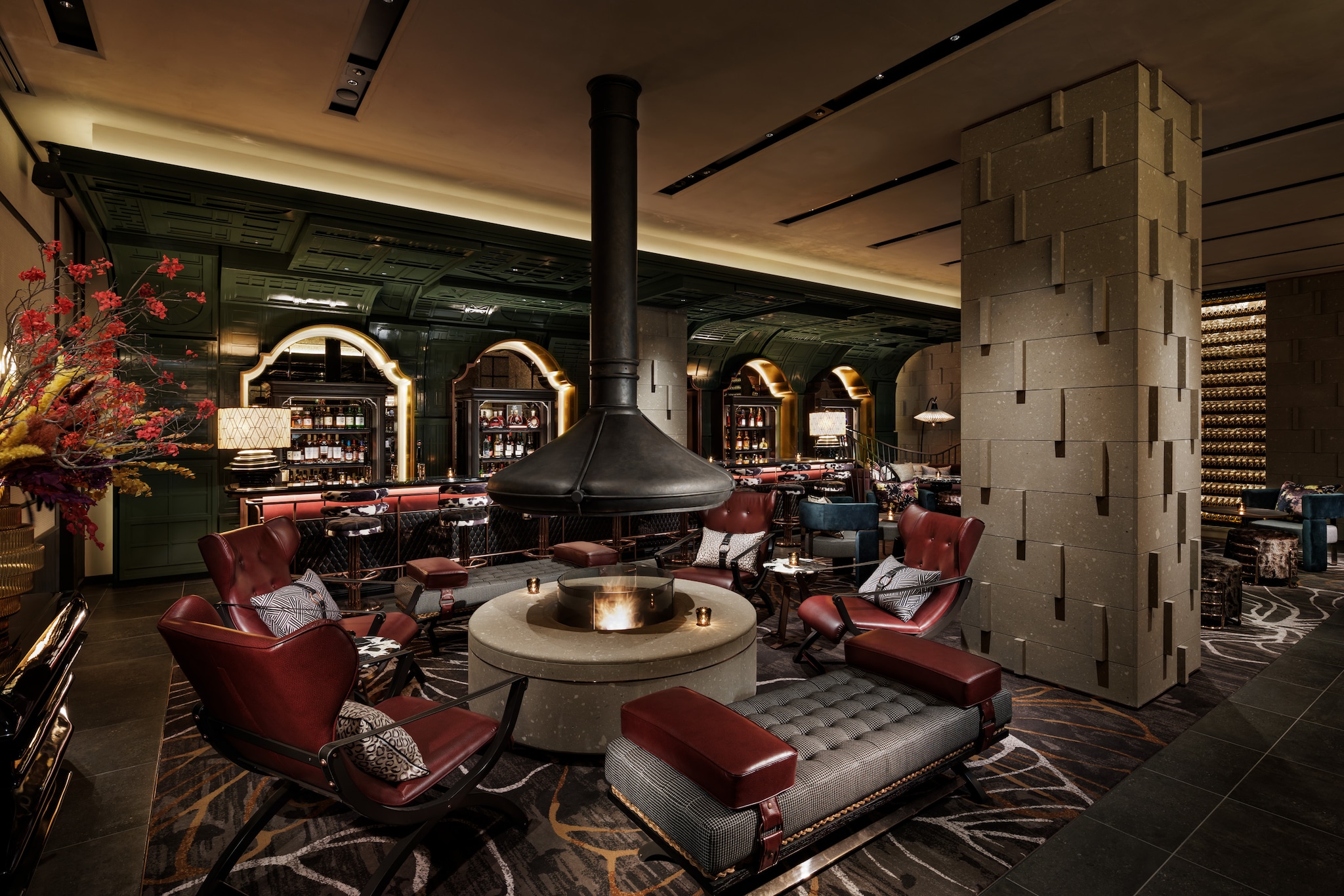 The circular fireplace at the bar lounge rests behind a gray barrier, under a smoke hood. Deep red leather chairs surround it. 