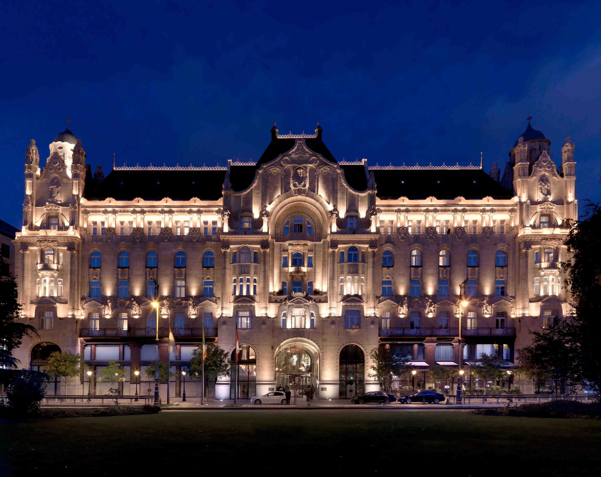 Exterior view of Four Seasons Hotel Gresham Palace Budapest at night, with a blue roof and white Art Nouveau façade lit from below.