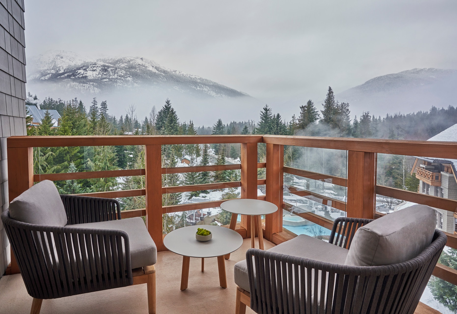 View from a Panorama Suite Balcony, arrayed with chairs and coffee tables. Beyond, hotel pools steam and forests lead to snowy mountains.