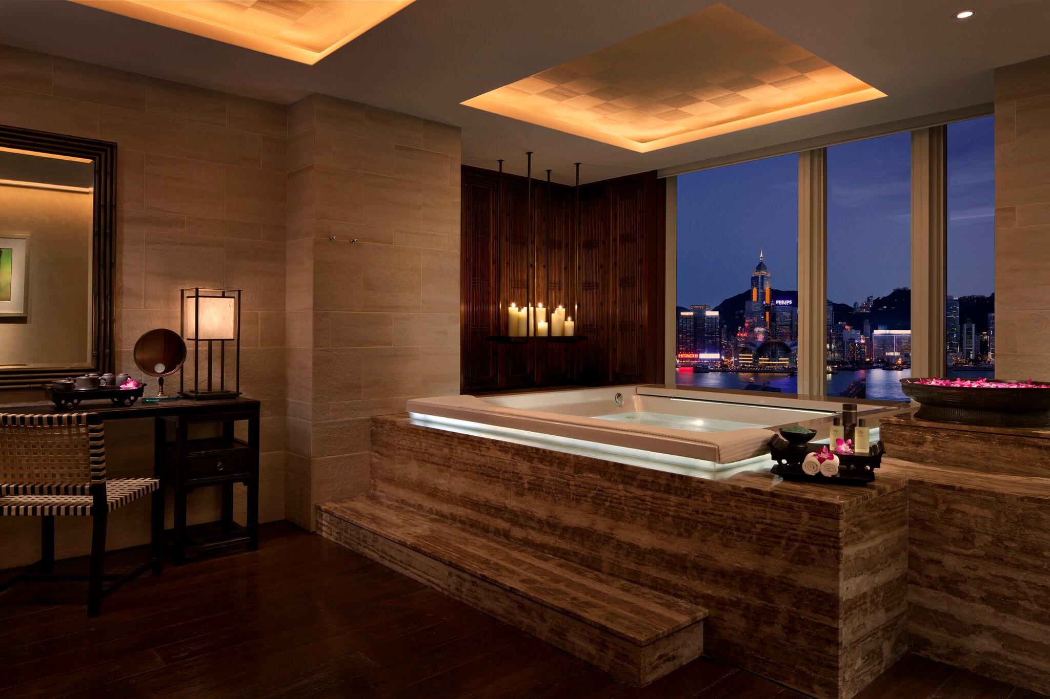 The couples suite in the Peninsula Spa features a hot tub in front of the windows overlooking the city. Pink flowers fill a bowl near the tub.
