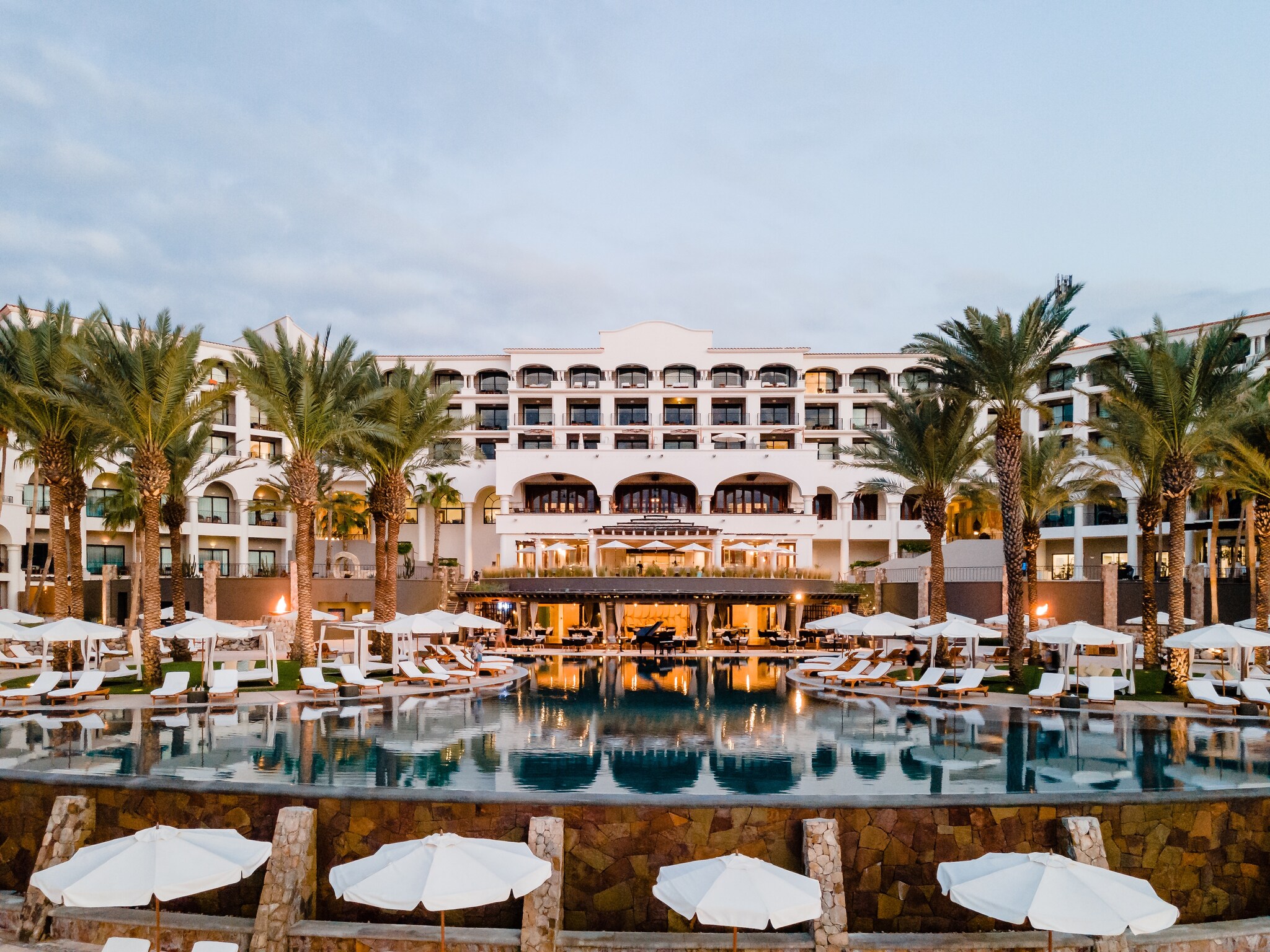 Exterior of Hilton Los Cabos, a grand white building with two wings to either side surrounding the central Jewel infinity pool.