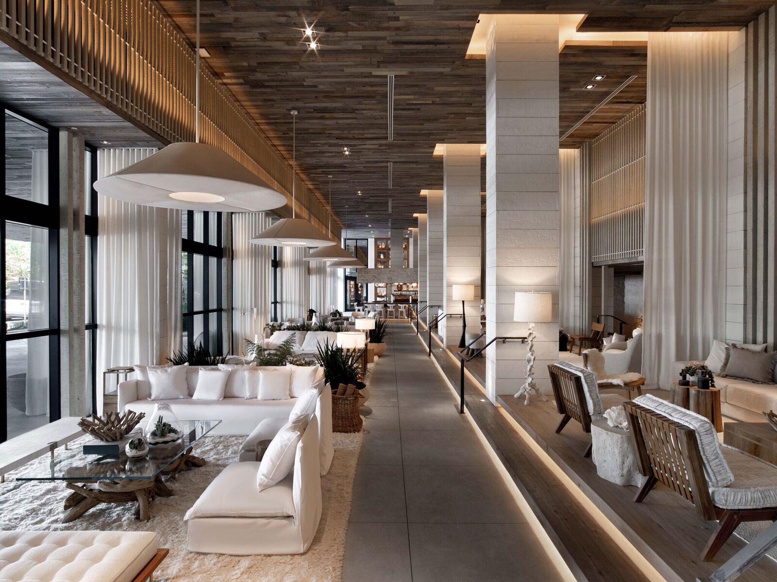 A long, open lounge area is filled with couches, tables, and chairs in neutral hues.