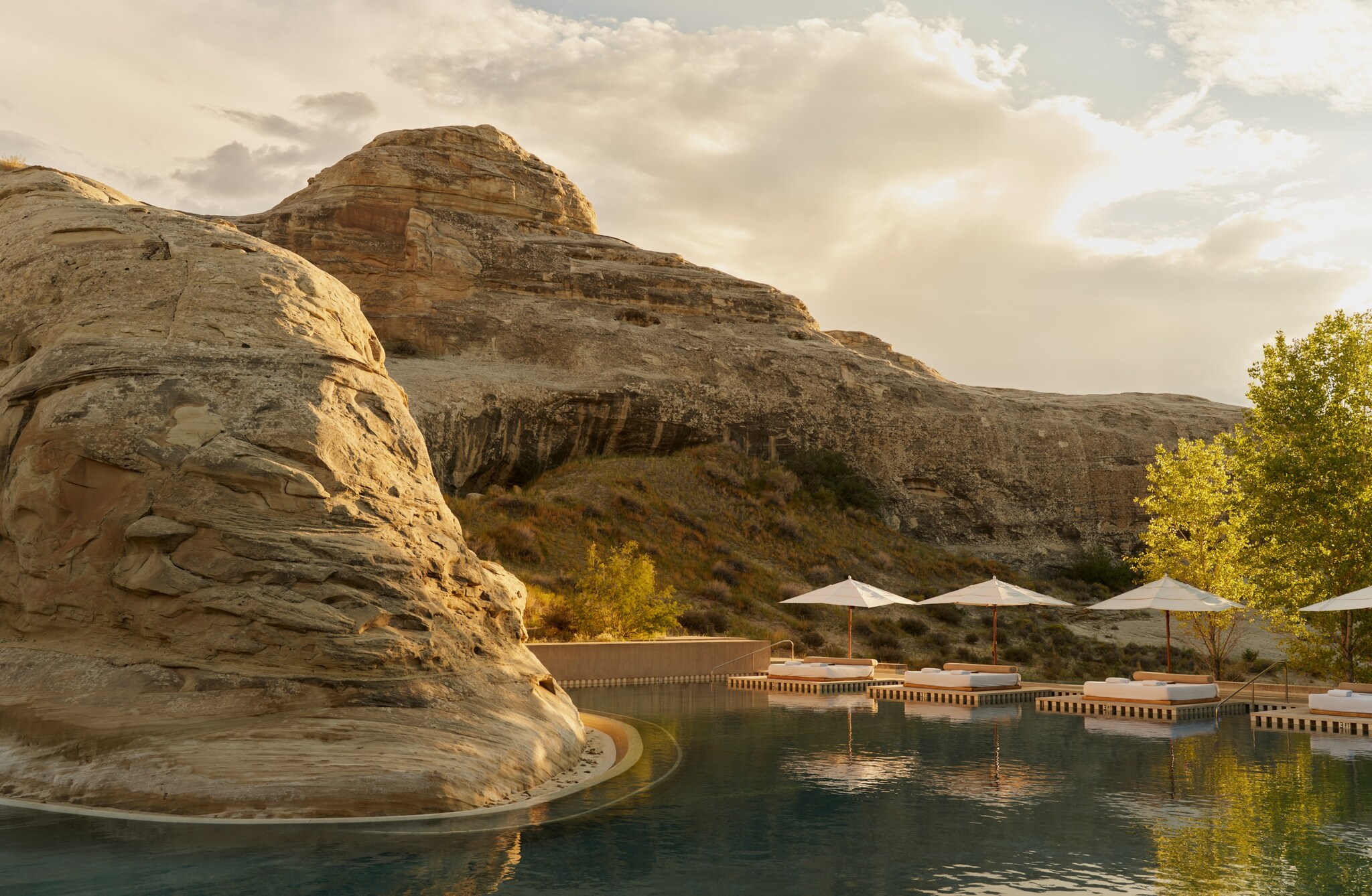 The Amangiri resort pool is interrupted by a curved hillside. Beyond the umbrellas and loungers on the deck, a rough desert landscape looms.