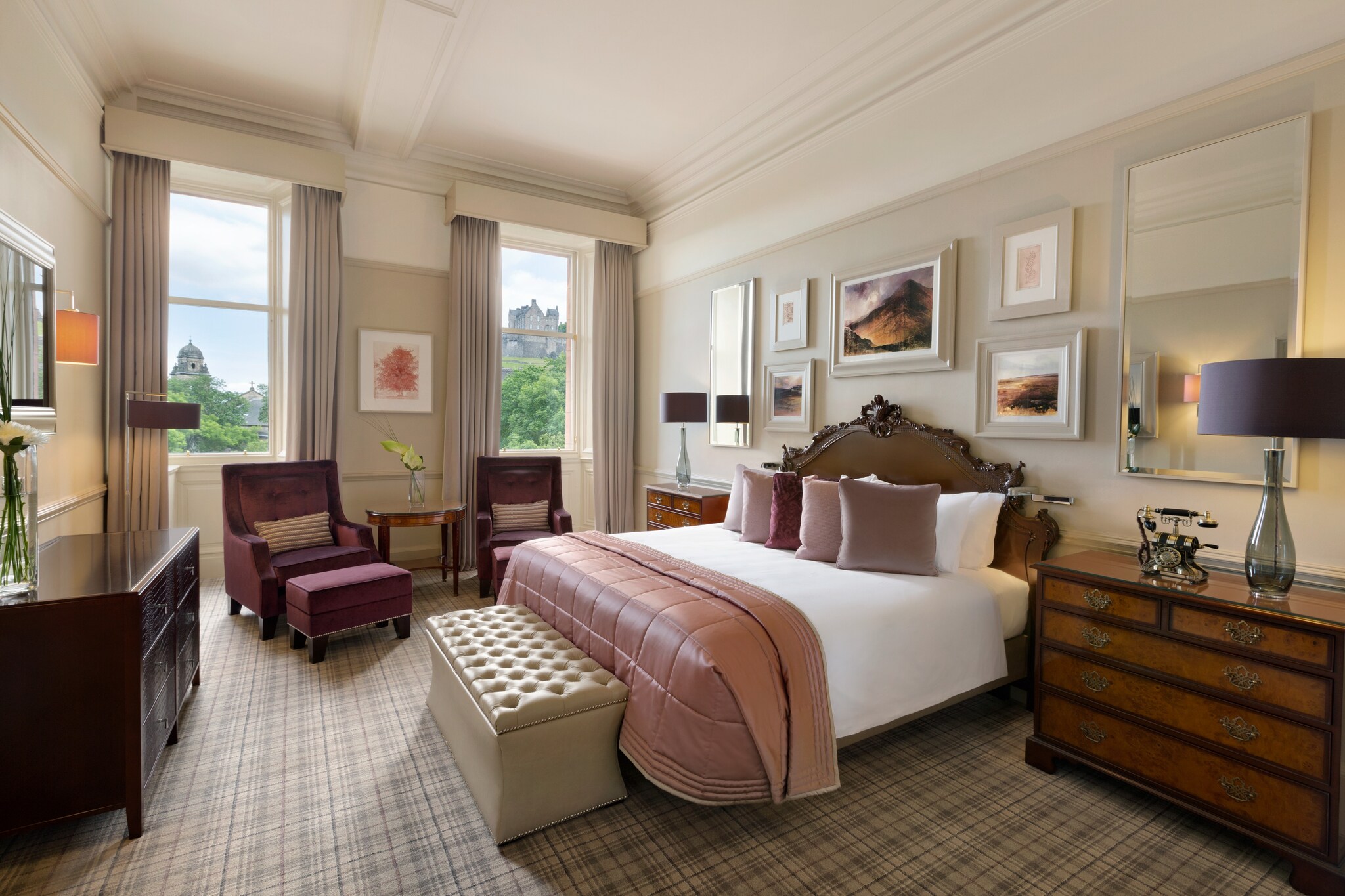 The Alexander Graham Bell suite of The Caledonian Edinburgh has tan walls lined with pictures, a plaid carpet, and pink cushions on the bed.