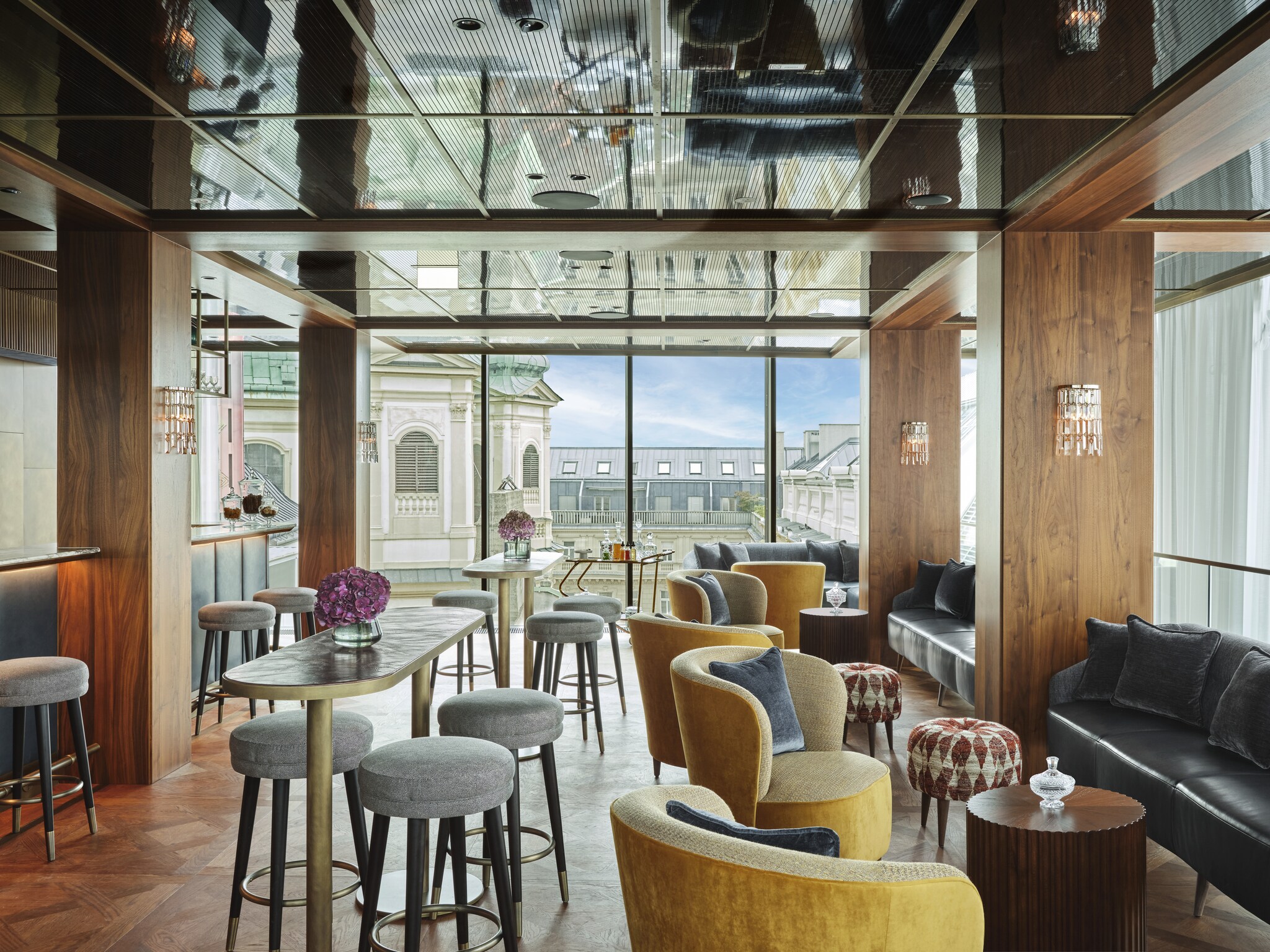 The rooftop brasserie Neue Hoheit Bar is filled with high-top tables, stools, and leather booths surrounded by floor-to-ceiling windows.