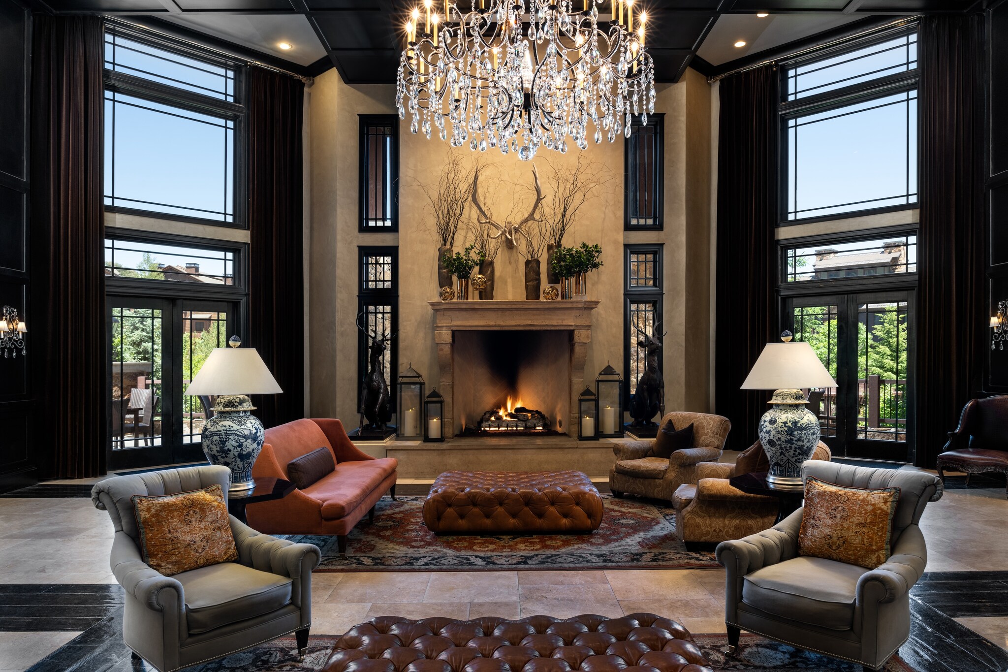 At the end of the hotel lobby, plush armchairs are arrayed around a large leather ottoman. Stag horns are mounted above a roaring fireplace.