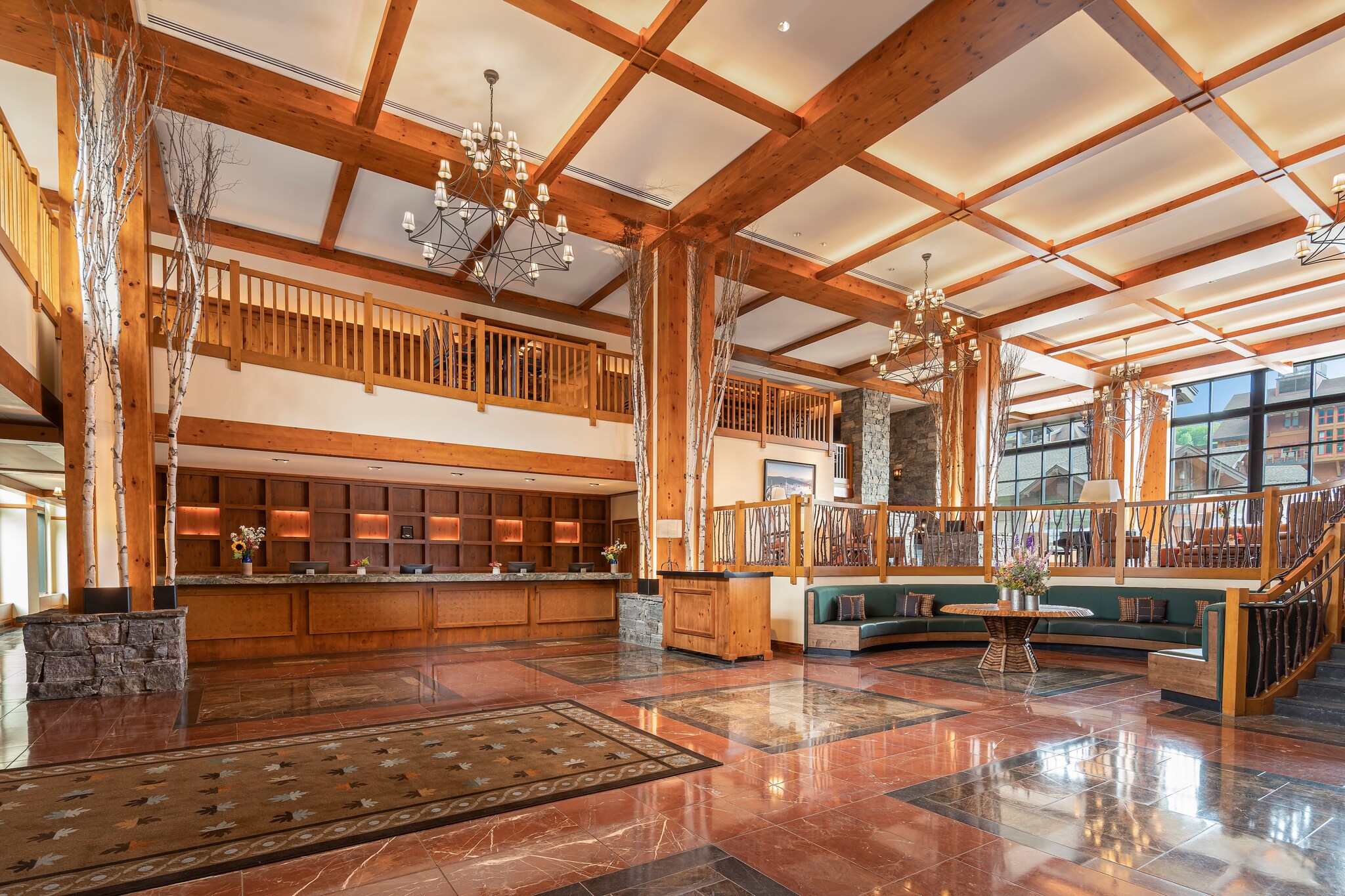 The expansive main lobby has red marble floors and exposed orange-brown beams. Potted birches line the white walls.