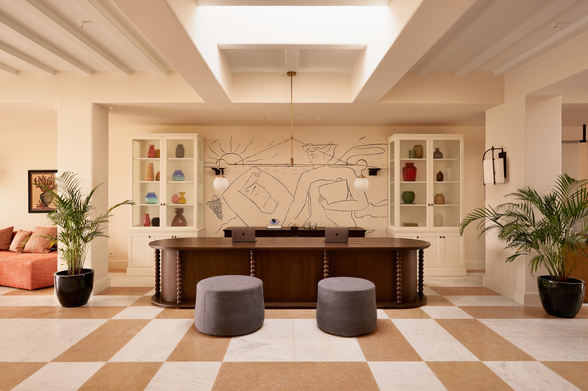 The front desk features a line-drawing mural of a couple stretching out on the beach. The room is airy, with white walls and potted ferns.