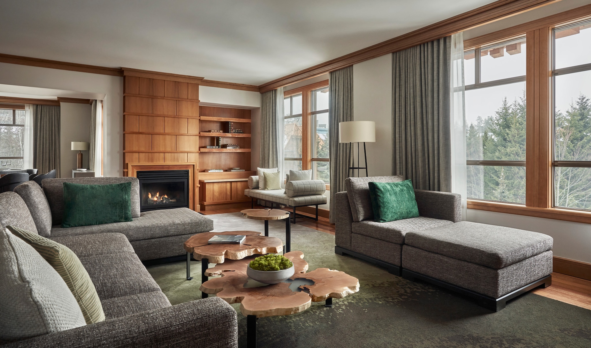 The living area of the Blackcomb Suite is arrayed with gray couches and coffee tables made of tree cross-sections, lit by wide windows.