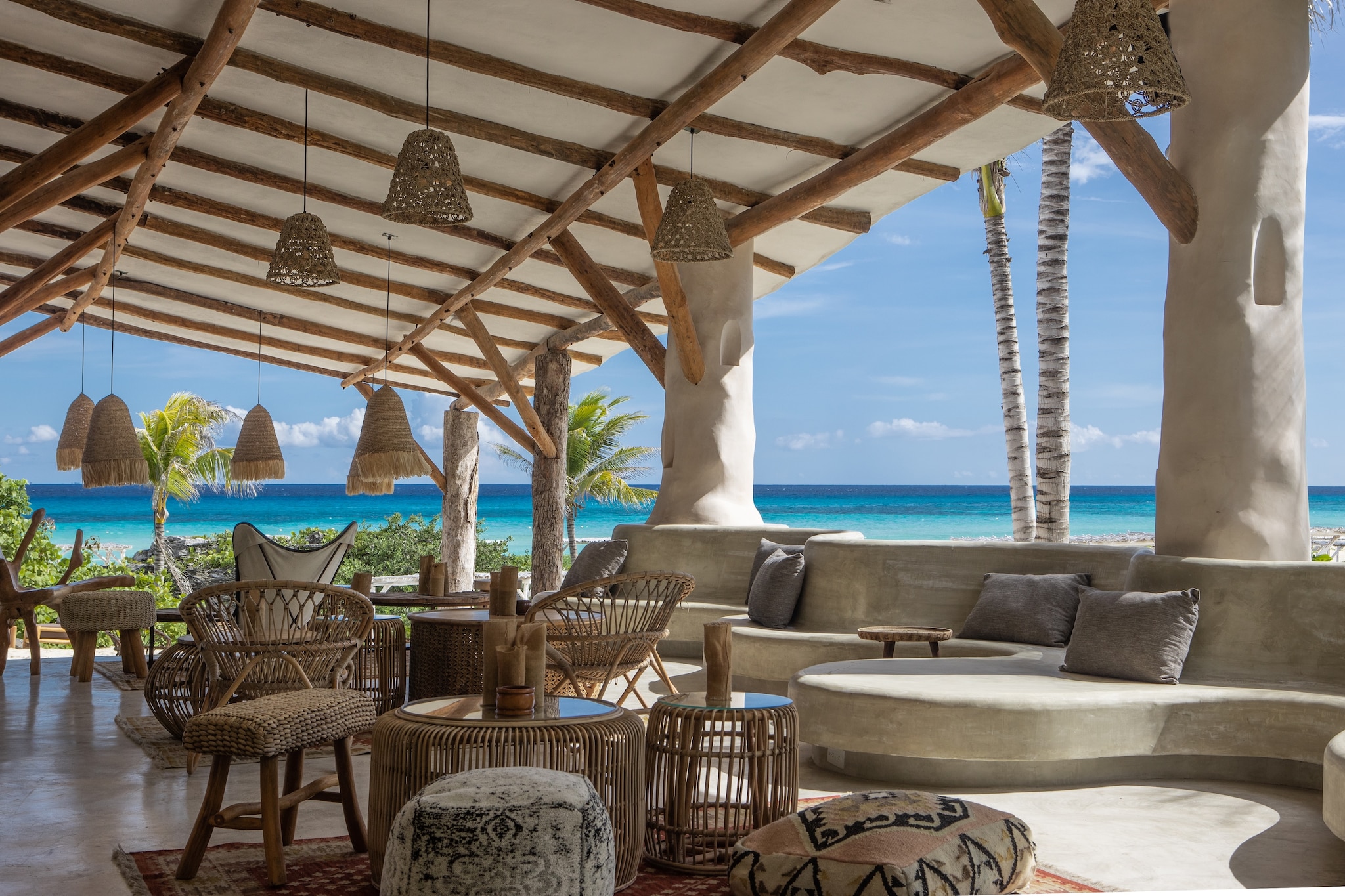 Eolo Beach Club is decorated with woven light fixtures and wicker furniture. The bright waters of the sea are visible through the open walls.