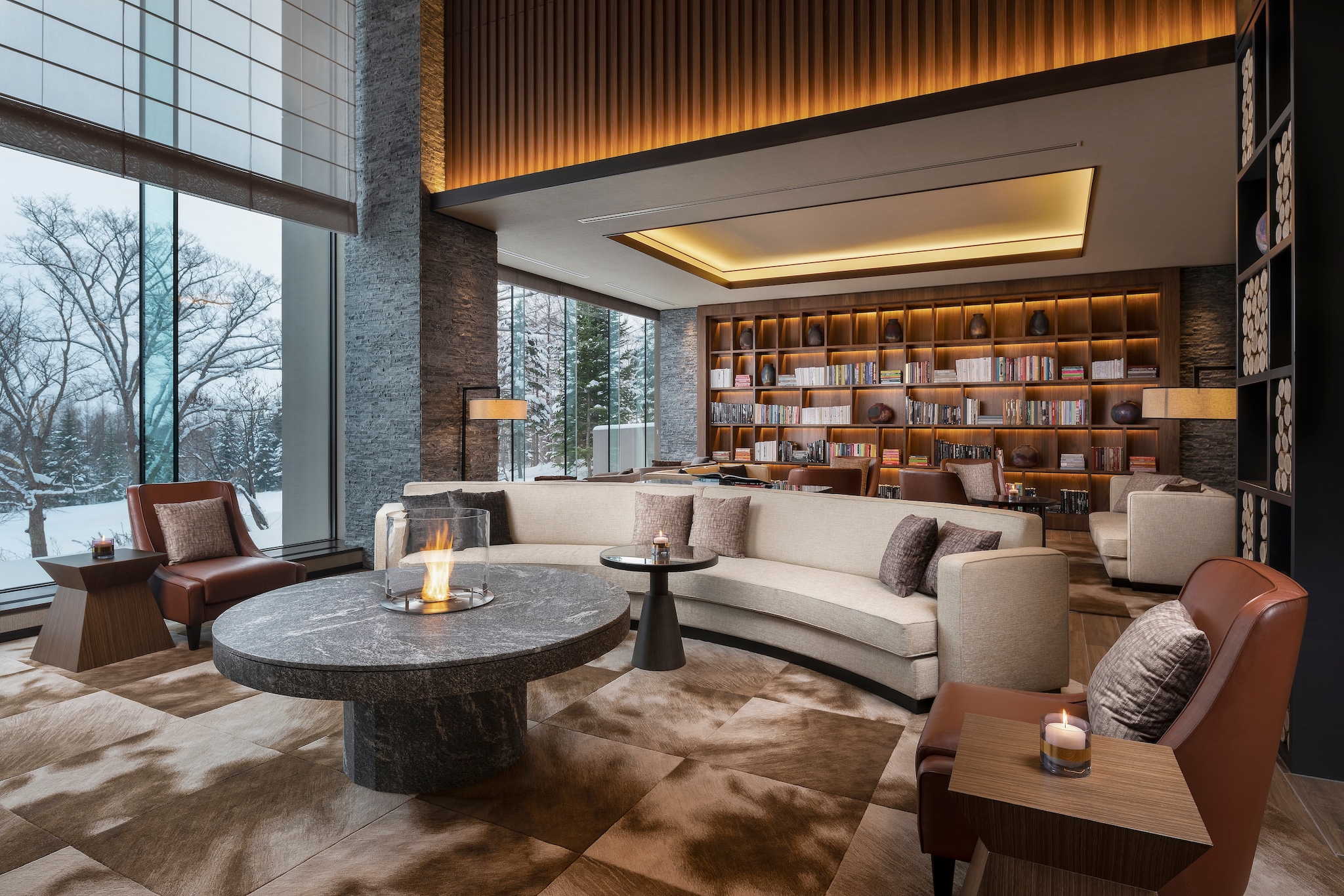 In Ume Lounge, a large, semicircular couch and brown leather armchairs are gathered around a circular table with a fire in the middle.