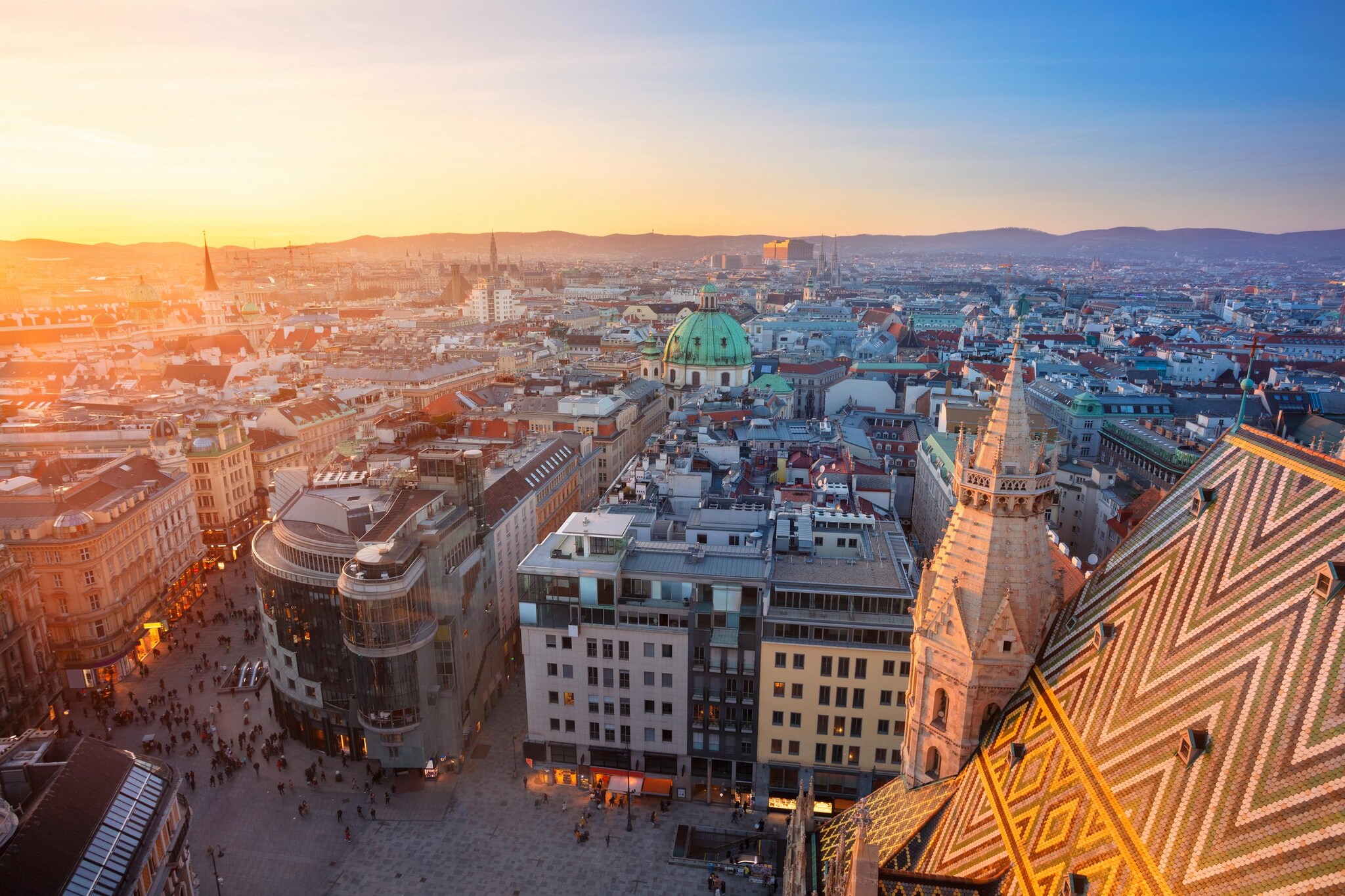 Aerial view past the gothic spire of St. Stephen’s Cathedral and over the rest of the domes and buildings of Vienna at sunrise.