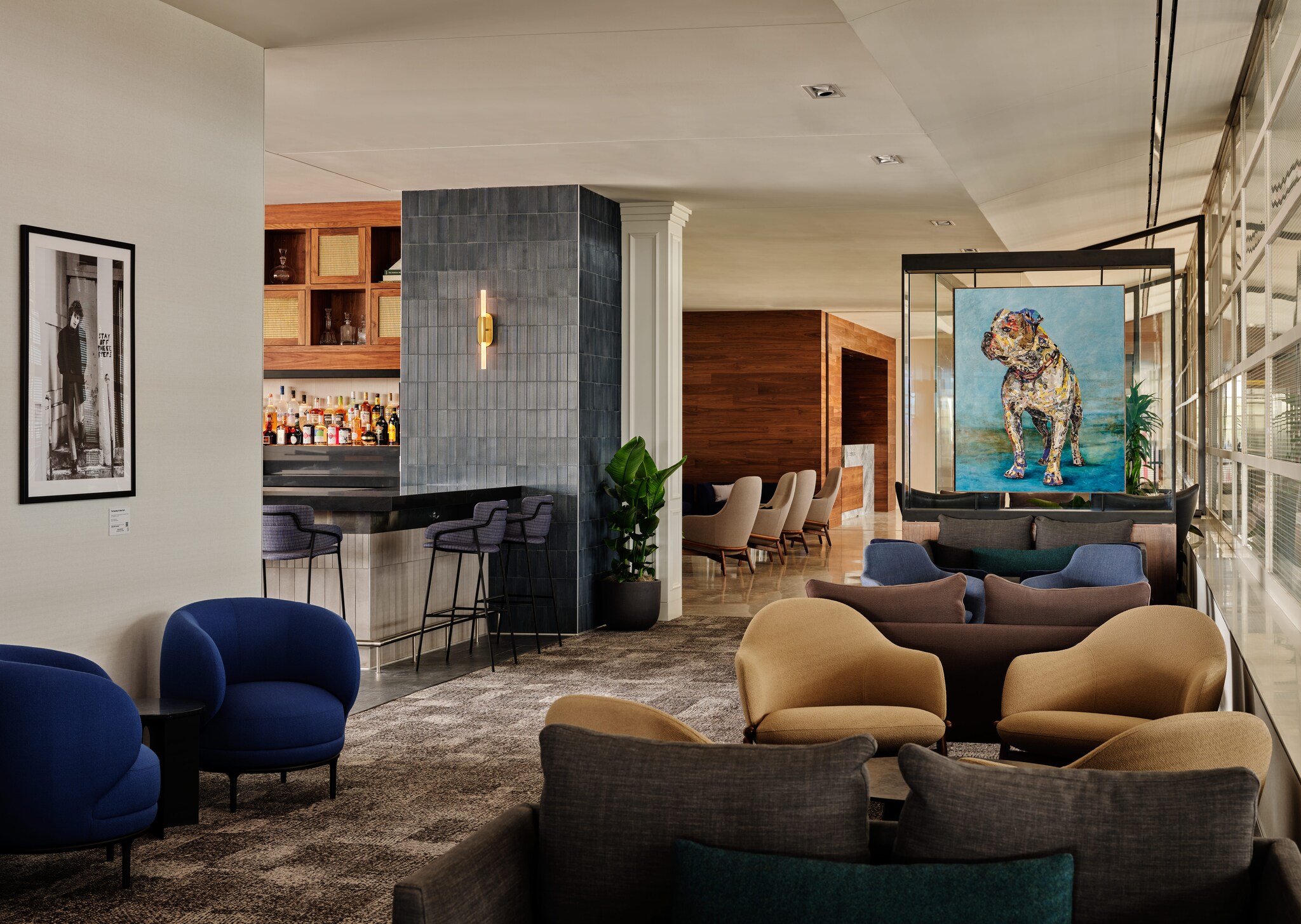 An airport lounge features extensive seating, a well-stocked bar, and a painting of a bulldog.