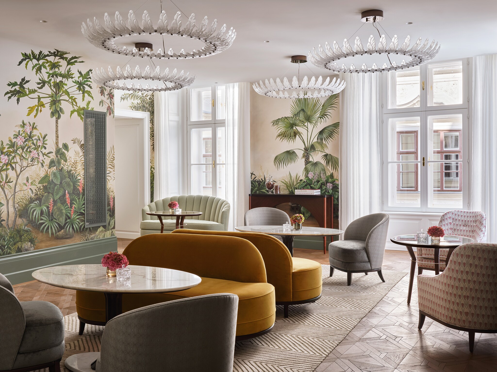 Salon Aurelie in Rosewood Vienna has blossom-like light fixtures and botanical murals, surrounding oval tables and slim-profile couches.
