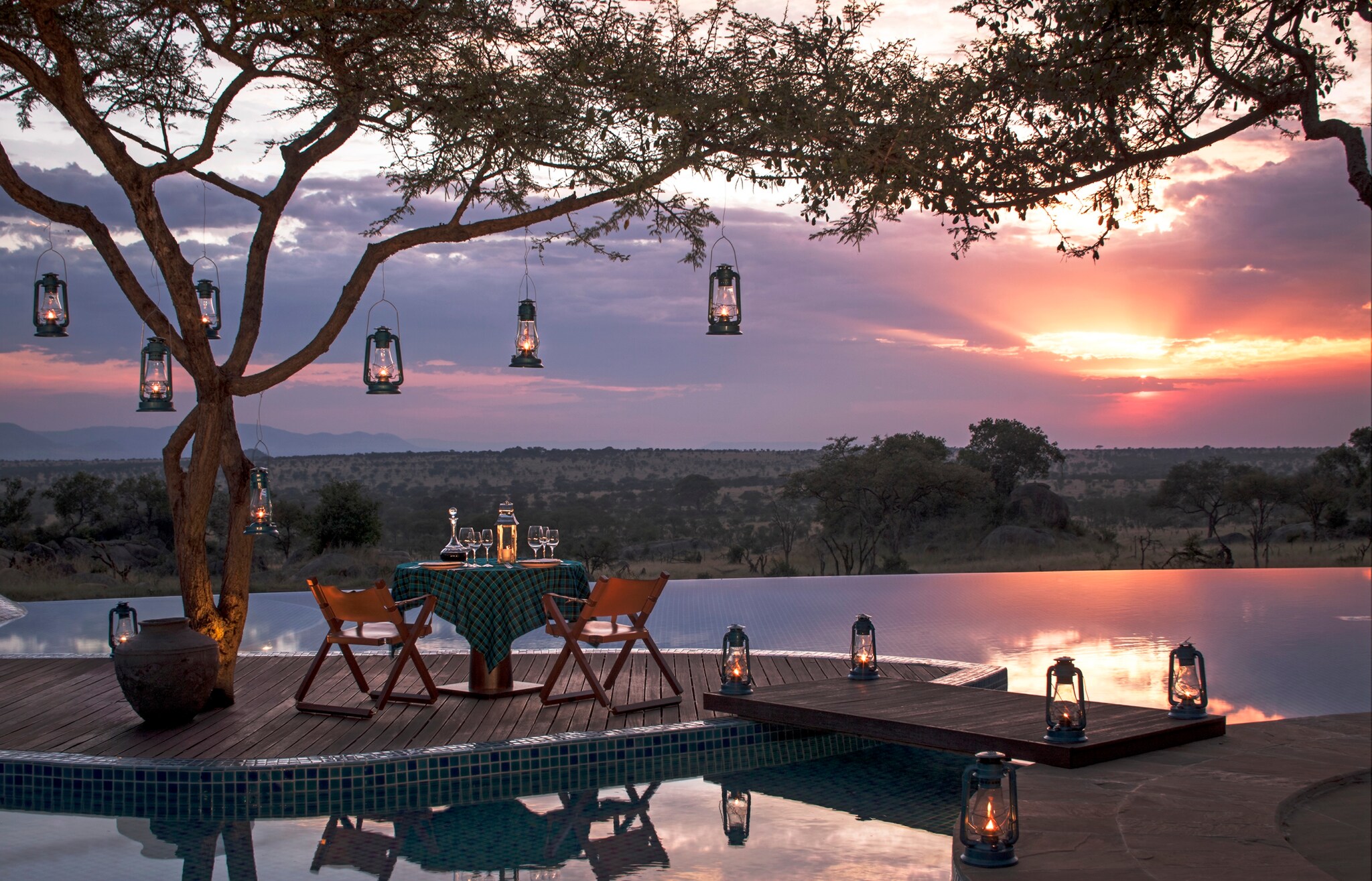 Sunset casts purple and orange light over a table set for two next to the pool. The tree above is hung with camp lanterns for soft light.