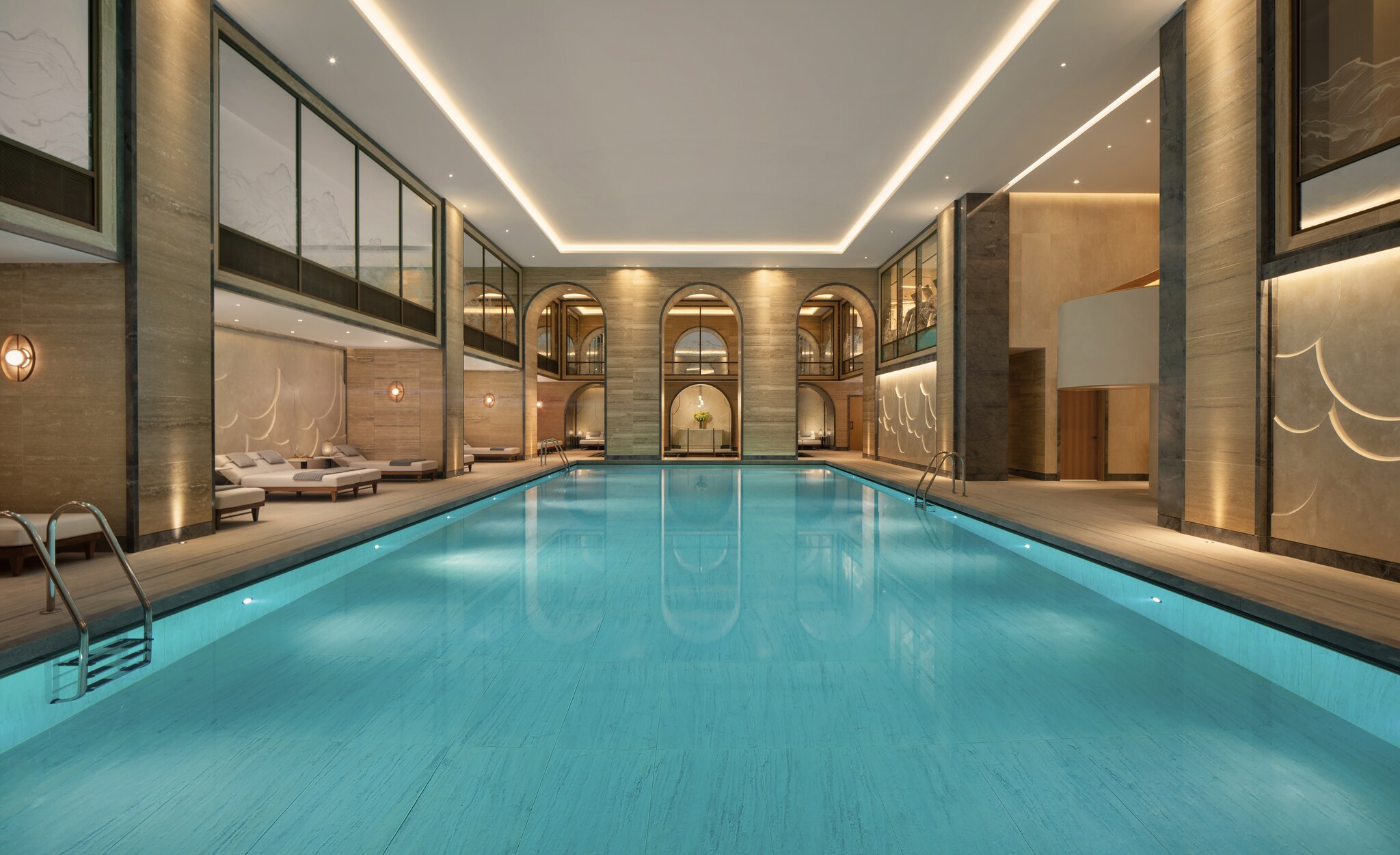 The indoor pool is rectangular, set in a high-ceilinged beige room with periodic alcoves containing low lounge chairs.